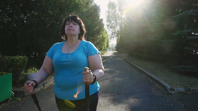 A woman walks through the Park with sticks for Nordic walking Sunny summer morning.