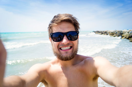 Hipster man on beach, smiling, taking selfie, sunny summer