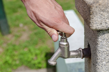 Hand opening water drip from water tap in park