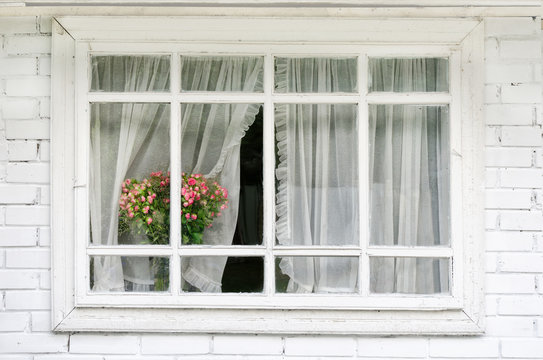 The horizontal white window with curtains, a bouquet of flowers on the windowsil