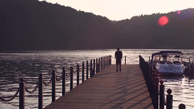 happy traveler hipster with backpack walking on pier at sunset shore near water, summer travel concept, slowmotion