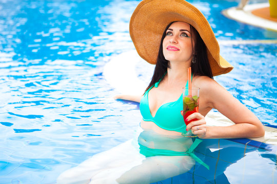 Beautiful brunette woman in bikini and hat, enjoying mojito cock