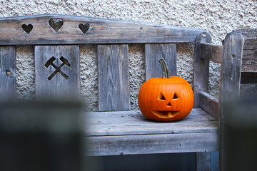 A pumpkin with a carved face on a bench during Halloween. 