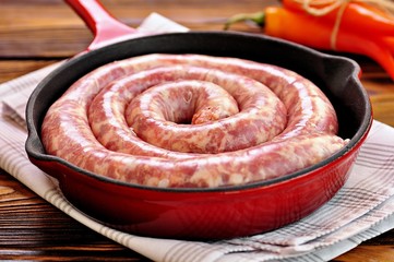 Raw pork sausage in a cast iron frying pan on a wooden background.