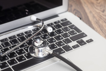 Medical stethoscope with a modern laptop computer on wooden back