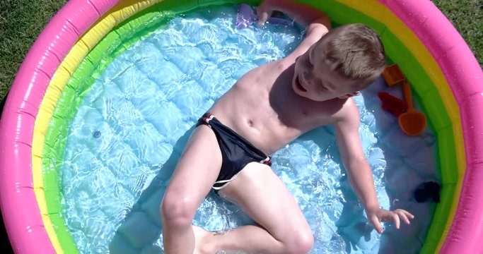 Boy Play and Having Fun in Inflatable Pool on Green Lawn in a Sunny Day