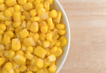 Organic sweet corn in a small bowl atop a wood table.
