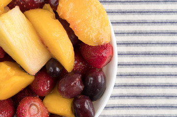Mixed fruit in a bowl on a tablecloth top view.