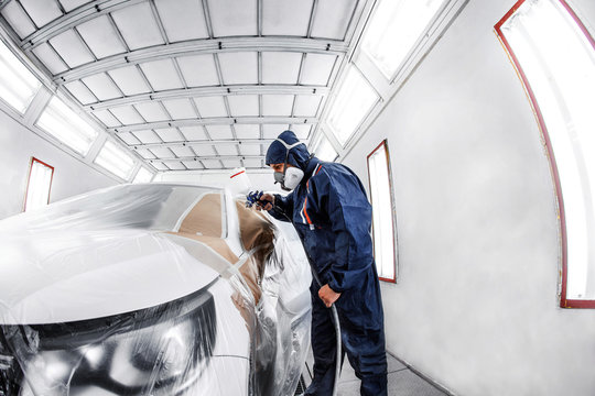 worker painting a white car in special garage, wearing costume and protective gear