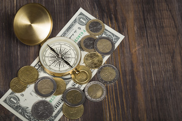 Compass with euro coins, dollar bill on wooden surface