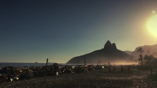 Beachgoers pack the shore as the sun sets behind the silhouette of Two Brothers Mountain at Ipanema Beach in Rio de Janeiro, Brazil