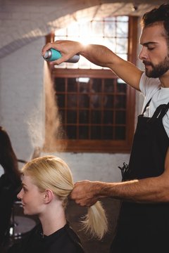 Male hairdresser styling customers hair with hair spray