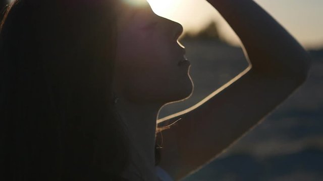 profile of pretty girl in the summer on the beach at sunset in slow motion