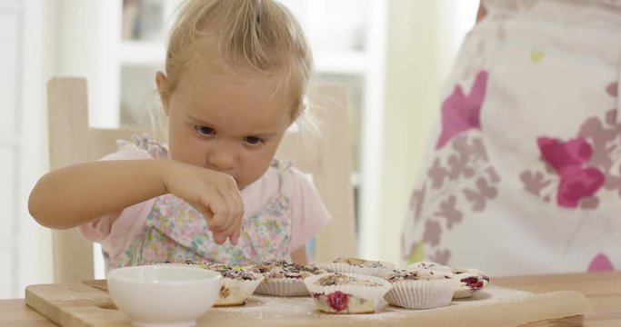Close up on serious little girl with short blond hair helping to prepare set of muffins on table