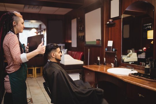 Female barber showing man his haircut in mirror
