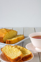 Madeira Cake Sliced on a Plate with A Cup of Tea on white wooden table with copy space vertical selective focus