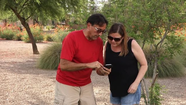 Two adults play a popular augmented reality smartphone game outside in a public park.