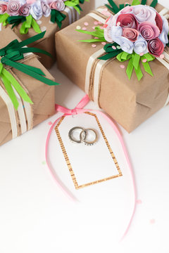 Gifts decorated paper pink flowers. Wedding rings in white gold.