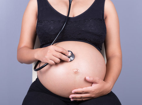 close-up of pregnant woman with stethoscope listening belly to b