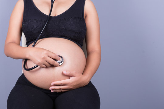 close-up of pregnant woman with stethoscope listening belly to b