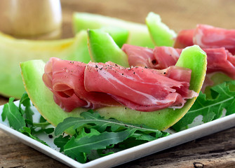 Melone mit Schinken - Rohschinken, auf Teller mit Rukola / Nahaufnahme - Makro / Foodstyling 
