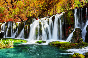 Fototapeta na wymiar Waterfall and azure lake with crystal water among fall woods