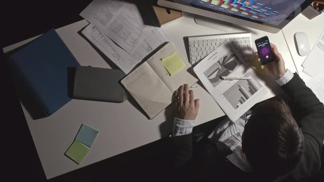 Top view of office worker working on documents with financial diagrams on it and swiping touchscreen to answer phone call