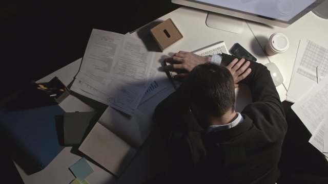 Directly above view of tired office worker sleeping on his table with papers and computer keyboard on it
