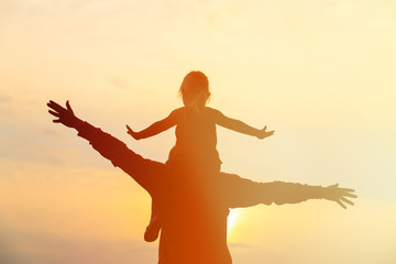 father and little daughter on shoulders play at sunset sky