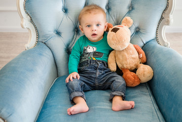 Little boy sits in sofa and plays his toy