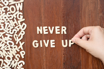 Word never give up made with block wooden letters next to a pile of other letters over the wooden board surface composition