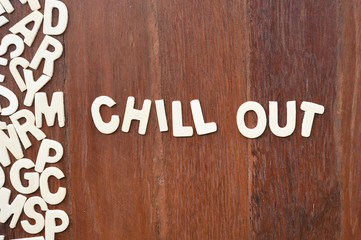 Word chill out made with block wooden letters next to a pile of other letters over the wooden board surface composition