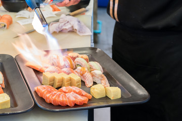 Torch burner over sushi rolls. Man's hand holding torch burner. Chef prepares uramaki sushi.
