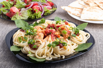 Closeup black plate with pasta and slices of braised chicken