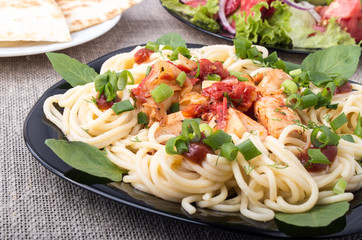 Closeup black plate with pasta and slices of braised chicken