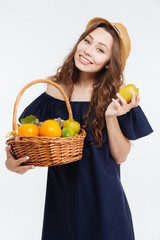 Obraz premium Cheerful cute young woman in hat holding basket with fruits