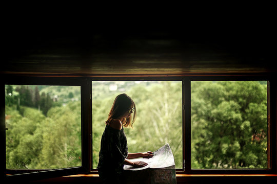 woman holding map sitting at window with view at amazing mountai