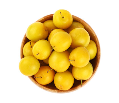 Fresh yellow plums in wooden bowl over white