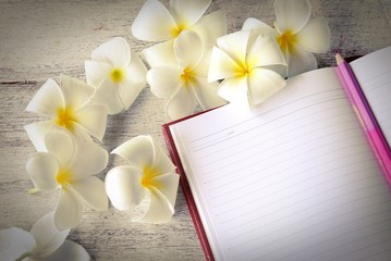 white plumeria flower and notebook on wood background in vintage tone 