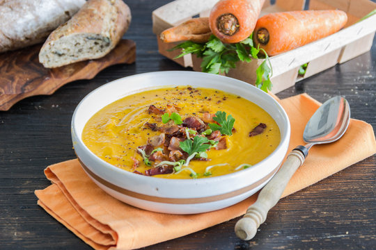 Roasted pumpkin and carrot soup with becon and pumpkin seeds on white wooden background