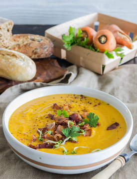 Roasted pumpkin and carrot soup with becon and pumpkin seeds on white wooden background