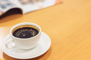 White cup of coffee with magazine on wood table.