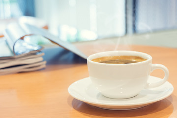 White cup of coffee with magazine on wood table.