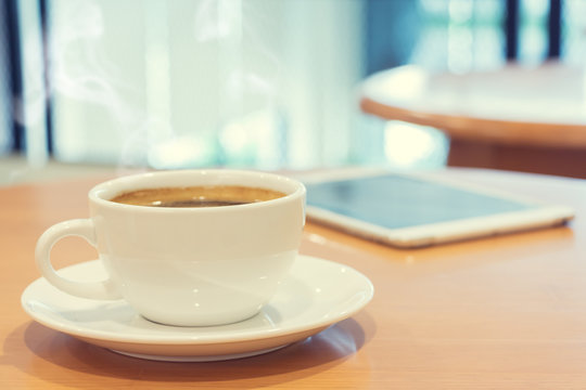 White cup of coffee with tablet computer on wood table.
