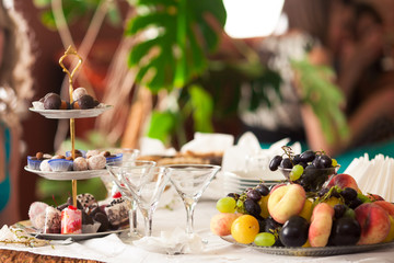 Fruits and sweets stand on the trays around empty glassware