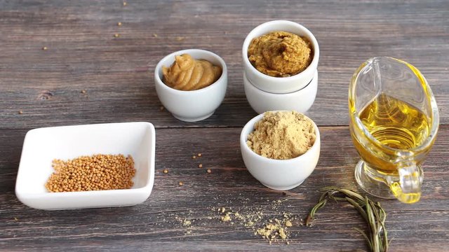 Set of different kinds of mustard - mustard seeds, mustard powder, french mustard, cremogenized and mustard oil - on wooden table.