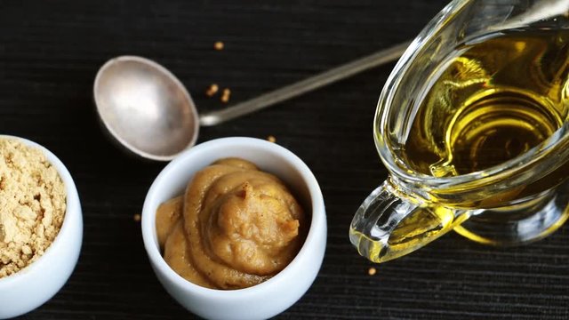 Set of different kinds of mustard - mustard seeds, mustard powder, french mustard, cremogenized and mustard oil - on wooden table.
