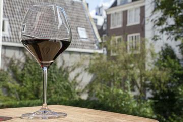 Obraz premium One wineglass with red wine and holland buildings in the day as background