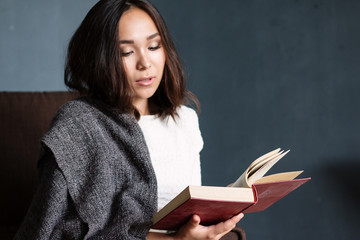 young,beautiful girl wrapped in warm plaid blanket reading book