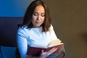 young,beautiful girl wrapped in warm plaid blanket reading book